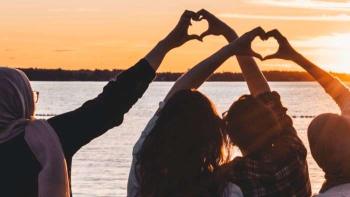 People make heart signs with their hands in front of the sunset.