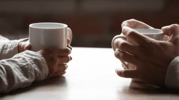 Two peoples hands holding mugs as they chat.