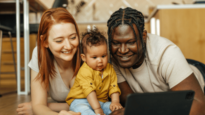 A family of people smile whilst watching an iPad.