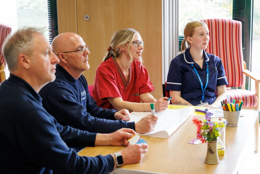 A group of healthcare professionals sit listening to a education trainer.