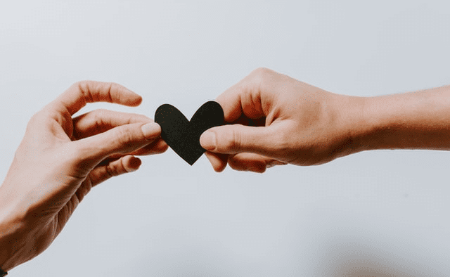 A paper cut out of a heart being shared between two hands.