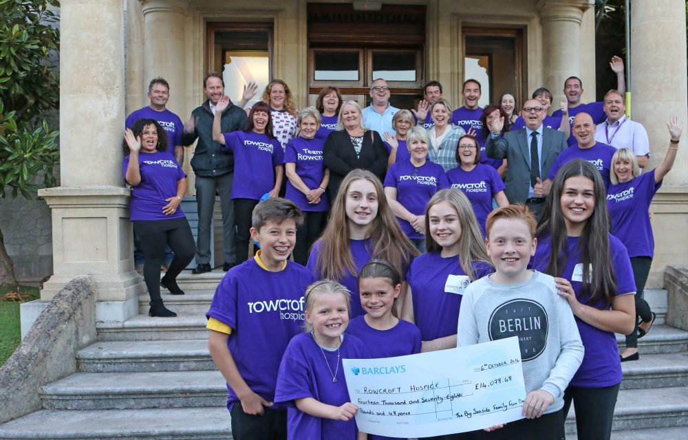 Community supporters stand outside Rainbow House, posing with a presentation cheque after a fun day of fundraising at a Rowcroft event.