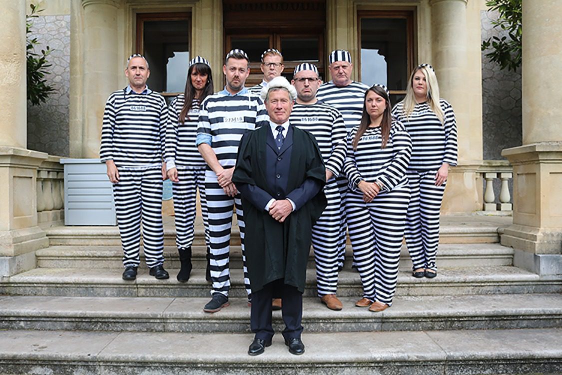 Eight local business stand with a judge dressed as convicts for Rowcrofts Jail or Bail fundraiser.