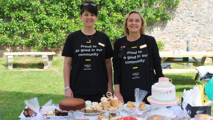 Marks & Spencer's corporate supporters stand in a garden, behind a table with lots of cake on it. Naturally, they're smiling.