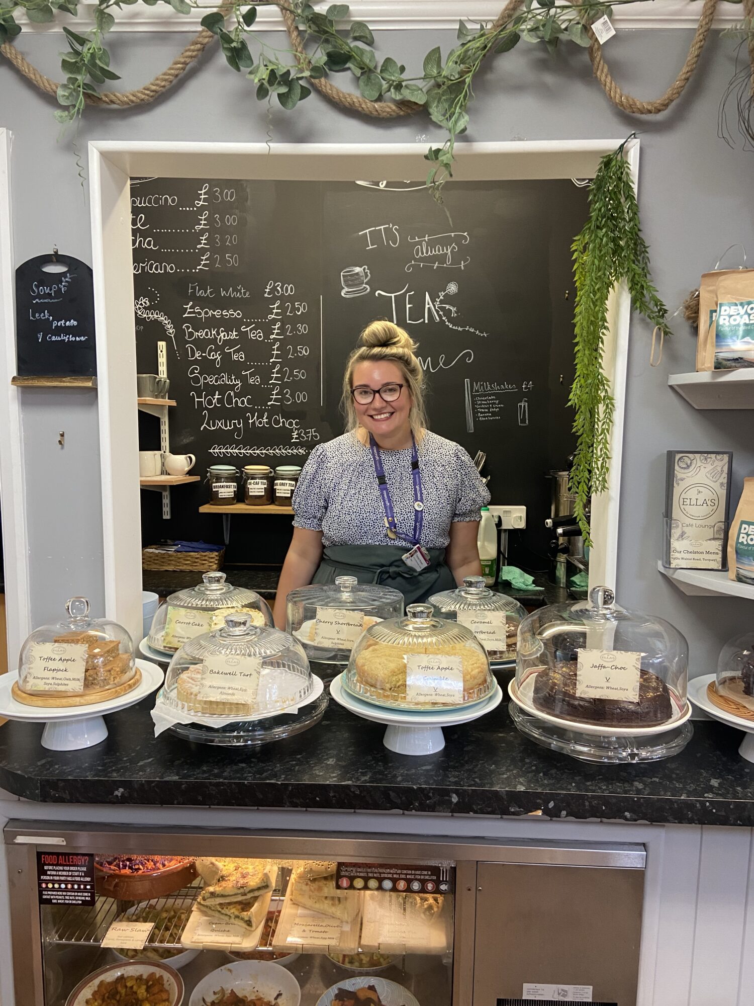 Chelsea smiles in front of a selection of cakes available at Ella's café.