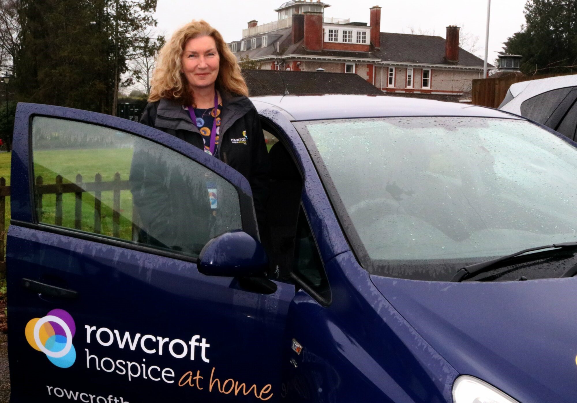 A Rowcroft nurse stands next to one of the Hospice at Home cars.