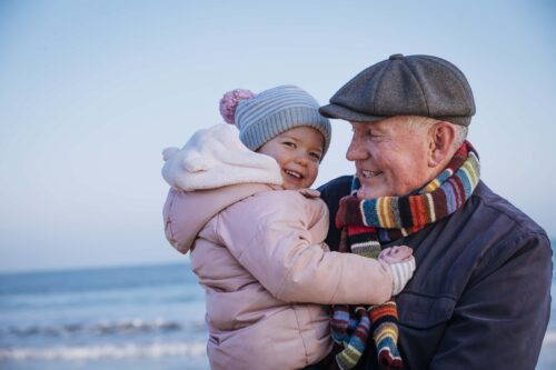 A grandfather hugs their grandchild. They're both smiling.