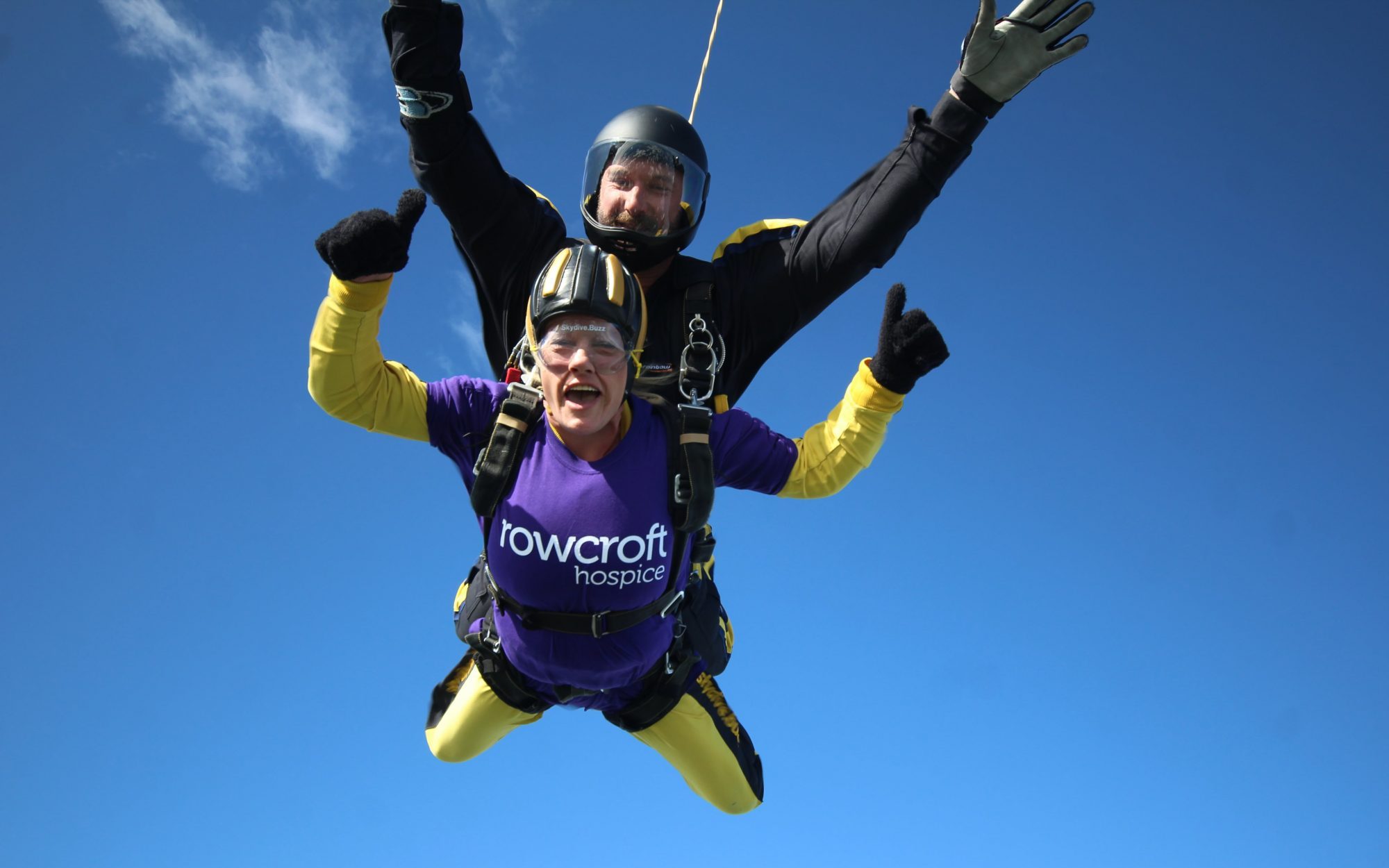 Fundraiser for Rowcroft poses with a thumbs up mid skydive.