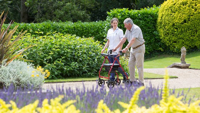 A nurse assists a patient walk through Rowcroft's gardens.