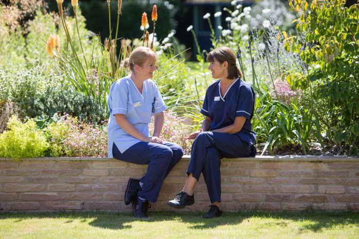 Rowcroft nurses in the hospice gardens facing each other talking and smiling.