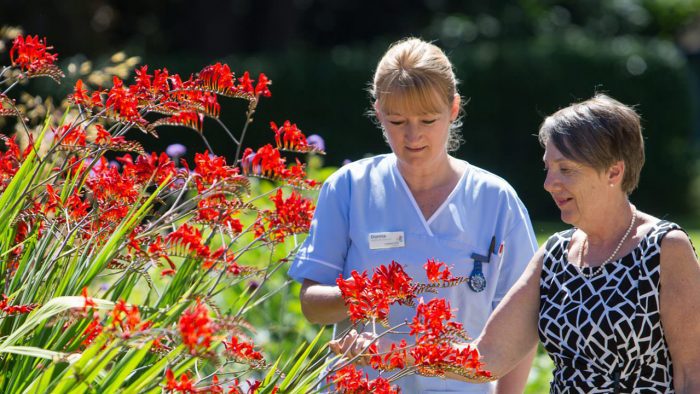 A nurse and a patient study a red flower in Rowcroft's garden.