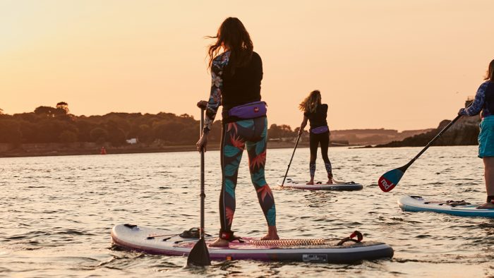 A group of women are seen paddle boarding at dusk.