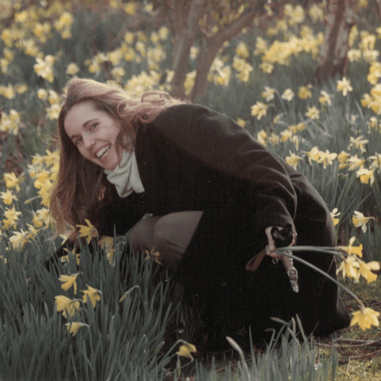A woman in a field of daffodils. She crouches, smiling.