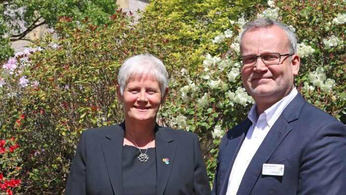 Trustee Sally and CEO Mark Hawkins stand outside in the beautiful gardens for a photo.