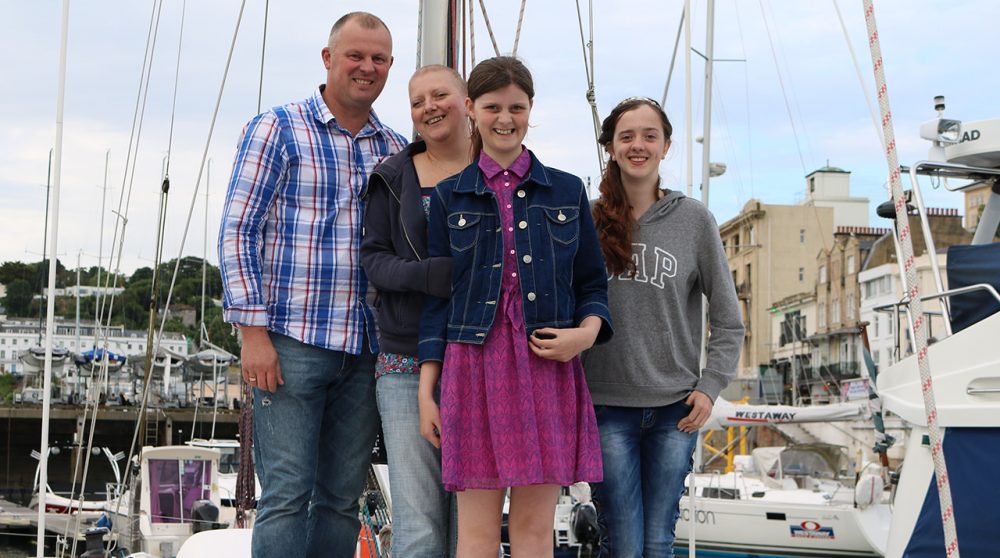 A family stood on their boat in Torquay harbour. everyone is smiling.