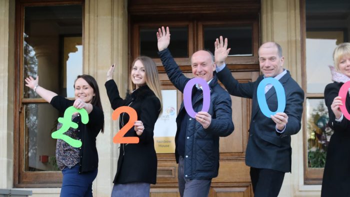 Fundraisers pose outside Rainbow House holding a sign that reads £2000.