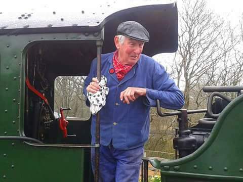 Dave poses on a steam train in a flat cap for a photo.
