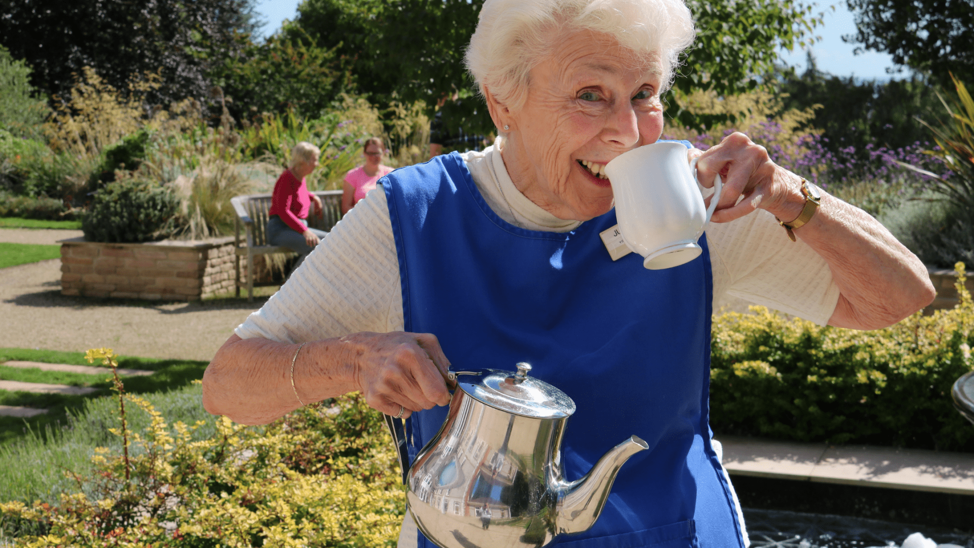A volunteer jokingly sips a cup of tea outdoors.